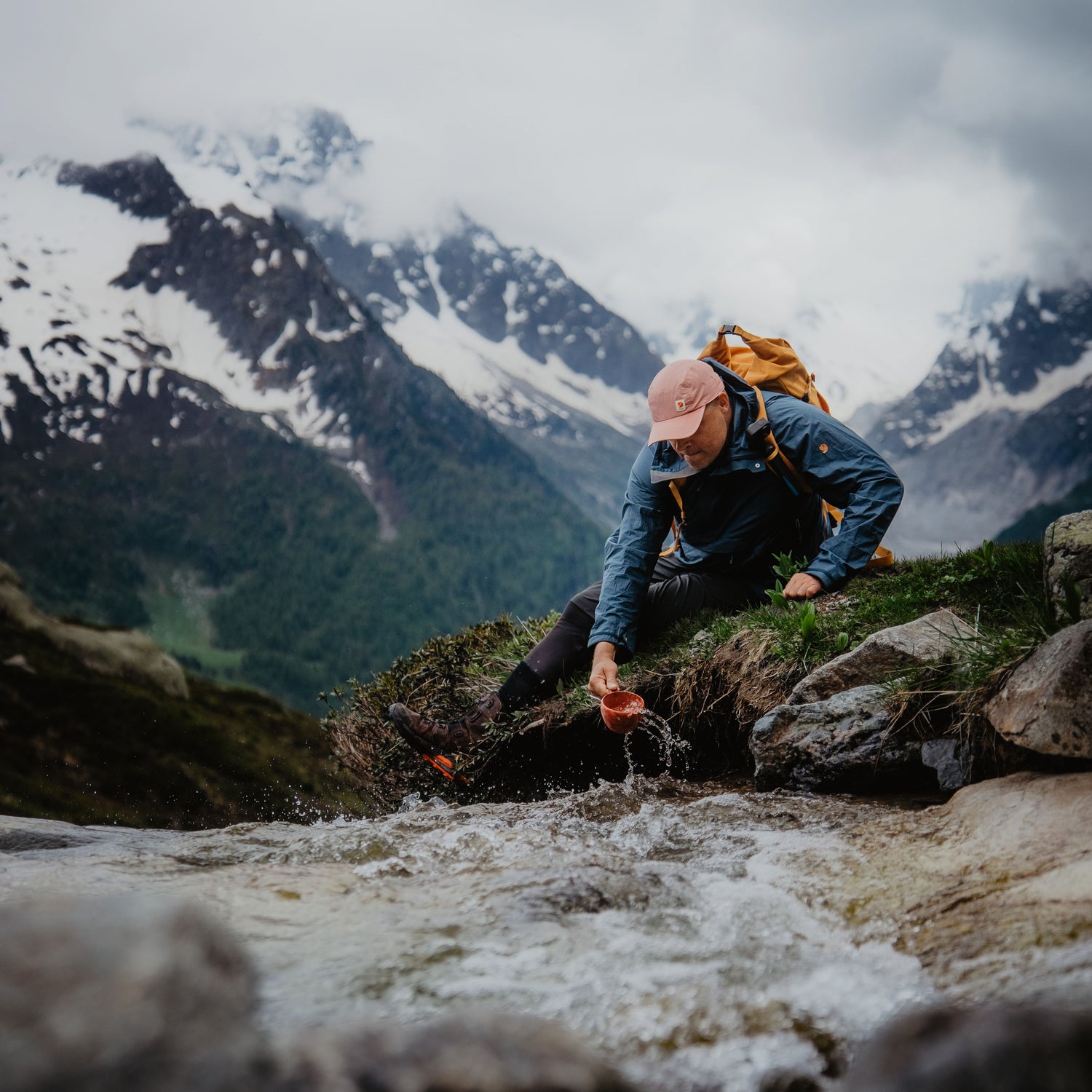 Man taking water with cup from river surrounded by snowy mountains